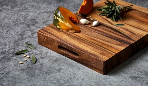 Wild Wood Mogo Chop Cutting Carving Serving Board with built-in handle, topped with pumpkin slices, garlic cloves, and fresh sage on a dark stone surface.