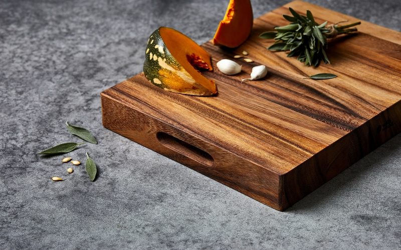Wild Wood Mogo Chop Cutting Carving Serving Board with built-in handle, topped with pumpkin slices, garlic cloves, and fresh sage on a dark stone surface.